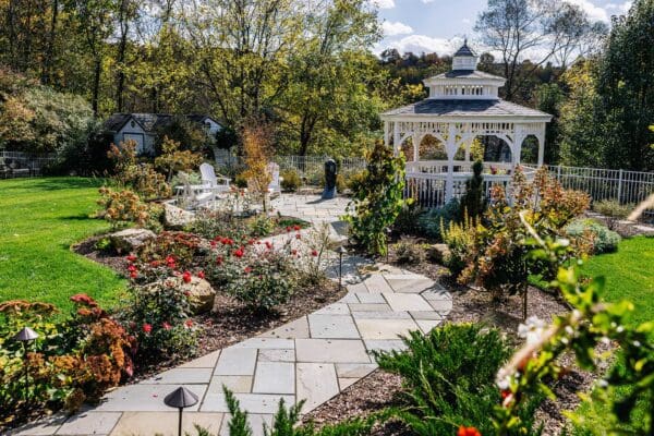 photo of landscape design install featuring a flagstone walkway leading down to a small patio with seating area under a gazebo.
