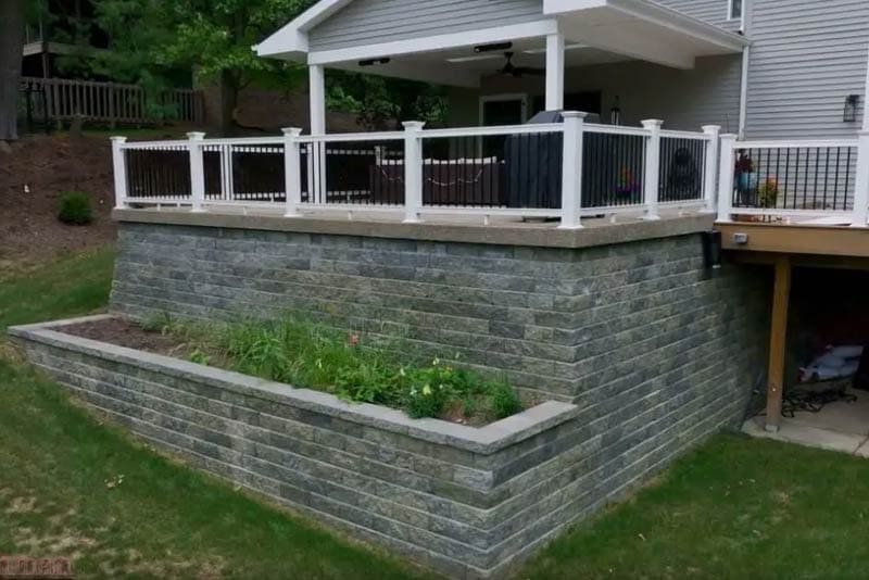 segmented retaining wall installation by Wichman Landscape that supports an outside deck and planter area